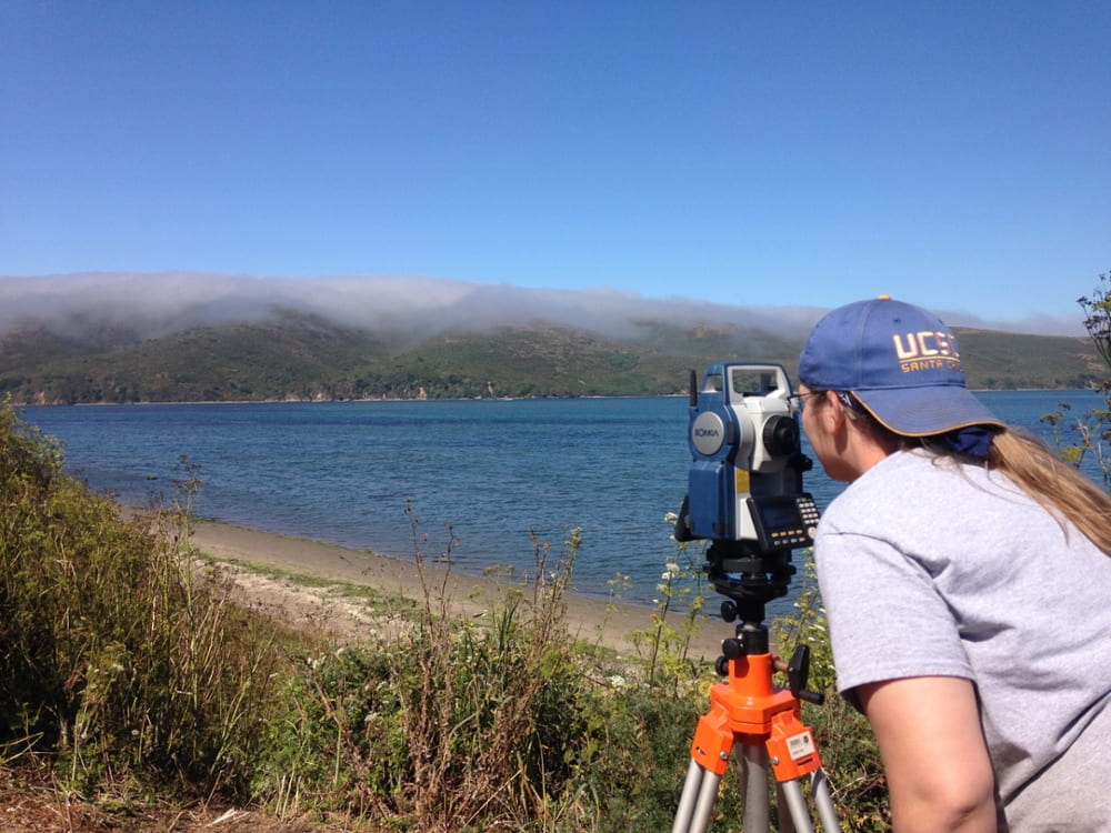 Surveyor measuring colonial marin with mountains in background and water in the foreground