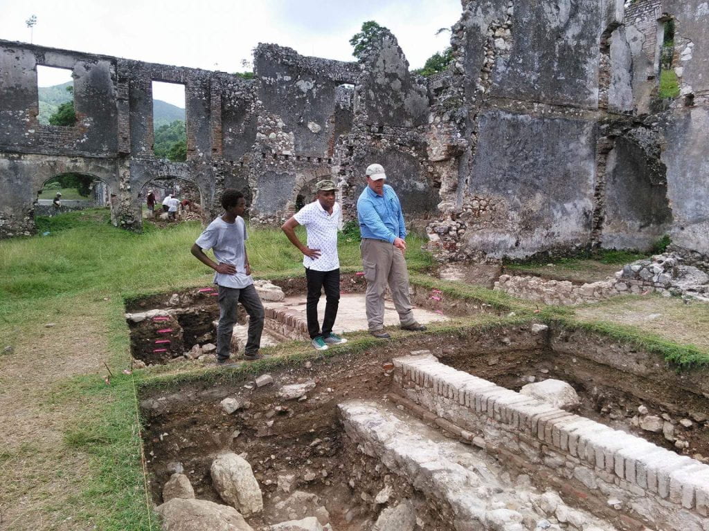 three people working on site in Haiti, one pointing toward a divider in the site
