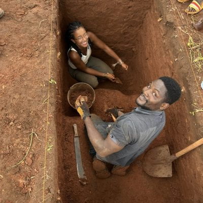 two students in the field, in a red clay pit, digging